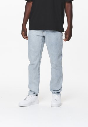 Helle blaue Denim-Jeans mit geradem Bein, ausgestattet mit einem klassischen Fünf-Taschen-Design. Getragen mit weißen Sneakern und einem schwarzen T-Shirt.