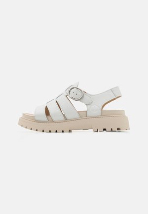 Sandalia de cuero blanca con tres correas horizontales, hebilla ajustable y suela de goma beige gruesa con un patrón texturizado.