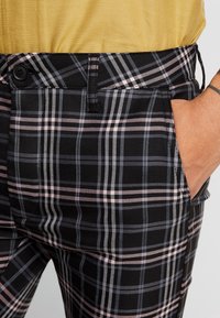 Svarta rutiga byxor med rosa och grå linjer, designade med sidficka och knäppning för säker passform. Strukturerad tyg.