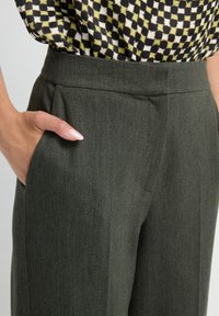Main dans la poche d'un pantalon tailleur gris foncé porté avec un chemisier à carreaux noir et jaune.