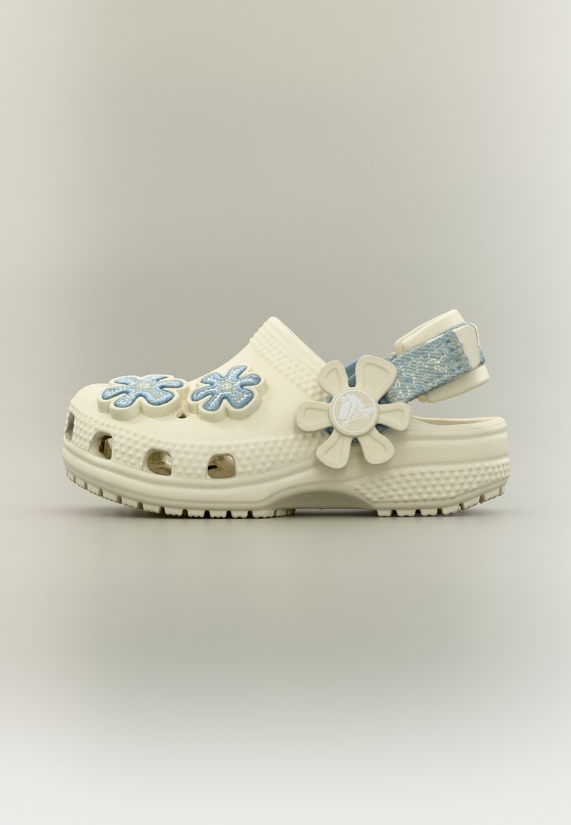 Sabot beige à enfiler avec des accents floraux bleus et une sangle de talon ajustable à texture denim, doté de trous de ventilation et d'une semelle texturée.