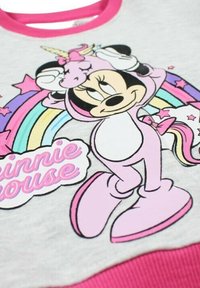 Sweat-shirt gris avec un col rose et un graphisme représentant un personnage de dessin animé, entouré d'un arc-en-ciel et d'étoiles aux couleurs vives.