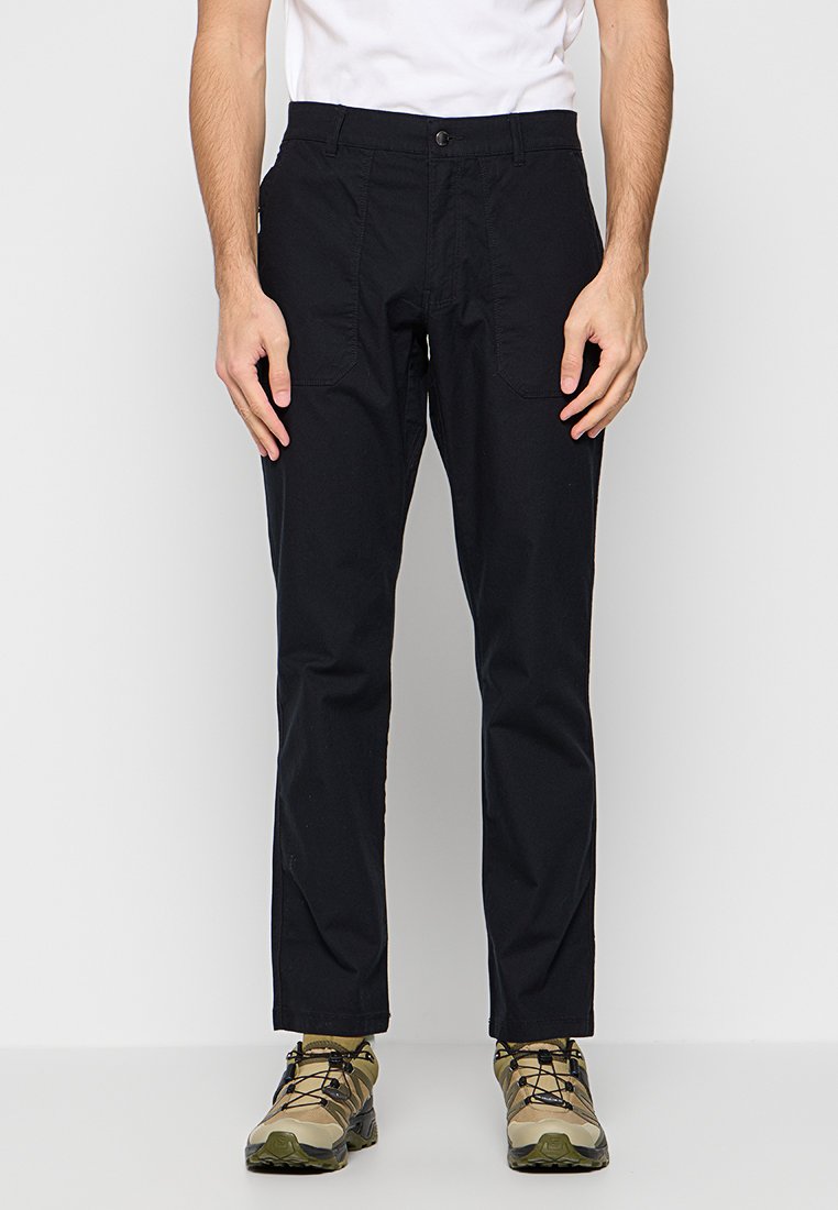 Schwarze, gerade geschnittene Hosen aus robustem Material, mit vorderen Taschen und Metallknopfverschluss. Getragen mit beigen Wanderschuhen.