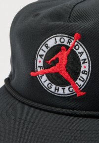 Μαύρο καπέλο βάσης με κεντημένο κόκκινο λογότυπο Jumpman μέσα σε κυκλικό έμβλημα «Air Jordan Night Club». Υφασμα με υφή.