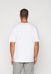Hvit bomull t-skjorte med en kontrasterende ribbestrikket hals i lilla og gul. Har korte ermer og en avslappet passform, med et NBA-logo på baksiden.