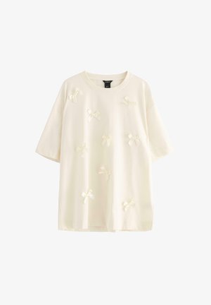 Kermakuvioinen puuvillapaita, jossa on lyhyet hihat ja joka on koristeltu pienillä, vaaleilla sulkilla edessä lisäyksinä.