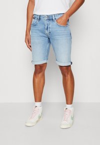 Ljusblå denimshorts med uppvikt fåll, femfickorsdesign och blekt struktur. Bärs med vita högskaftade sneakers och vita strumpor.