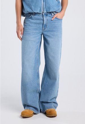 Lichtblauwe wijde spijkerbroek van denim, met een hoge taille en subtiele vervaging, gecombineerd met tan enkellaarzen.