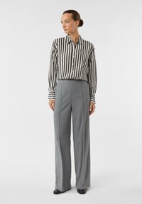 Koszula w pionowe czarno-białe paski zapinana na guziki, zestawiona z wysokim stanem szarych spodni o gładkiej fakturze i szerokich nogawkach.