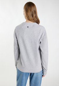 Sudadera gris con un corte relajado, mangas raglán y cuello redondo. Presenta un pequeño detalle de logo en la parte posterior y puños acanalados.