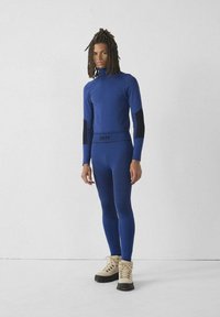 Blauw sportief shirt met lange mouwen en nauwsluitende broek met gestructureerde details, gecombineerd met beige laarzen. Zwarte accenten op mouwen en tailleband.