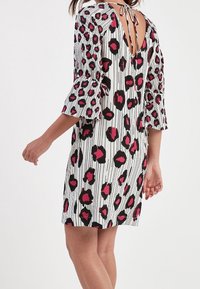 Robe blanche avec des rayures verticales noires et des taches de léopard roses, présentant des manches évasées et un dos ouvert maintenu par un lien.