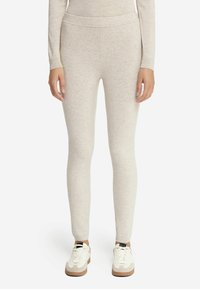 Leggings en tricot beige clair avec une texture lisse, une taille haute et une coupe ajustée, associés à des baskets blanches avec des accents beiges.