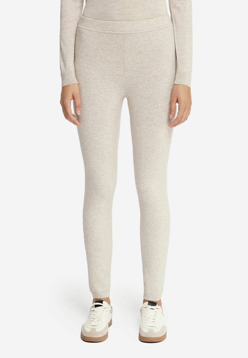 Leggings en tricot beige clair avec une texture lisse, une taille haute et une coupe ajustée, associés à des baskets blanches avec des accents beiges.