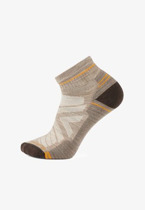 Beżowa skarpetka do kostki z brązowym noskiem i piętą, ozdobiona pomarańczowymi paskami i teksturowanym geometrycznym wzorem na górze.