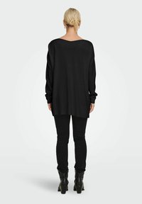 Czarny, oversize'owy sweter z długimi rękawami, ściągaczami i szerokim dekoltem, zestawiony z czarnymi obcisłymi jeansami i botkami za kostkę.