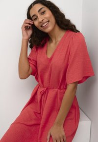 Robe en lin corail avec un décolleté en V et de courtes manches à volants, cintrée à la taille par un lien, avec un tissu texturé.