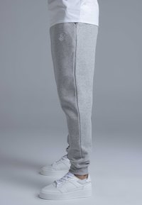Gray jogger pants with a stretchy waistband and side pockets, featuring a subtle embroidered logo in white. Paired with white platform sneakers.