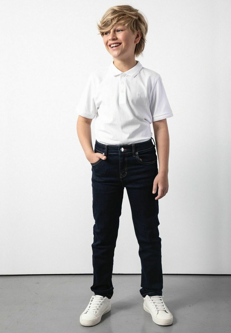 Biała koszulka polo z krótkim rękawem, granatowe dżinsy i białe sneakersy. Outfit ma klasyczny krój i casualowy styl.
