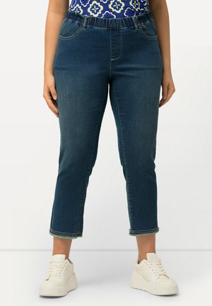 Jean capri en denim bleu foncé avec une taille élastique, des détails cousus et un ourlet effiloché. Assortis avec des baskets à plateforme blanches.