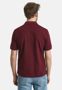 Bordeaux polo shirt met een zachte textuur, korte mouwen en een klassieke kraag, gecombineerd met lichtblauwe jeans, gezien vanuit de rug.