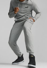 Ensemble en sweat-shirt gris et pantalon avec une poche kangourou, des chevilles à poignet, et des logos Puma noirs, associé à des baskets noires.
