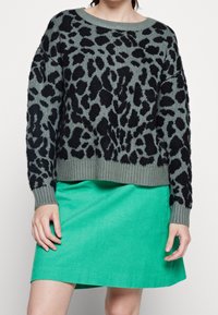 Svart och grön leopardmönstrad tröja med ribbat nederkant och ärmslut, tillsammans med en enfärgad grön kordkjol. Tröjan har en avslappnad passform.