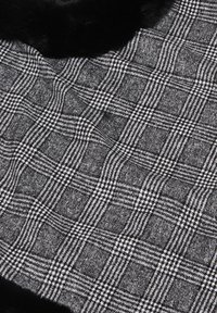 Tessuto a scacchi bianco e nero con una texture morbida, caratterizzato da un bordo con un accento peloso nero. Presenta un design a motivi.