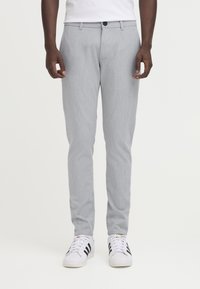 Pantaloni grigi chiaro su misura in tessuto liscio, con vestibilità dritta, passanti per cintura e chiusura con un solo bottone. Abbinati a sneakers bianche.