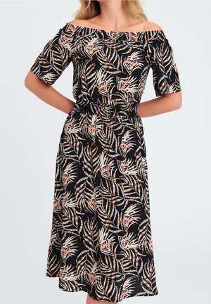 Schwarzes schulterfreies Midikleid mit Pfirsich-, Weiß- und Braunfarbenem tropischem Blattmuster und kurzen Ärmeln, getragen von einer Person mit Händen in den Hüften.
