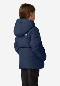 Námořnická pufovaná bunda s kapucí, se strukturovaným designem a logem na horní části zad. Měkká, zateplená látka, délka k pasu.