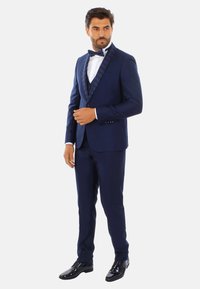 Tuxedo blu navy con revers a scialle a fantasia, camicia bianca, papillon nero e scarpe eleganti nere lucide. Vestibilità su misura e design elegante.