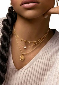 Trois colliers en or à plusieurs couches, mettant en avant un pendentif avec un design d'arbre, une perle et des chaînes délicates avec de petits accents en or.