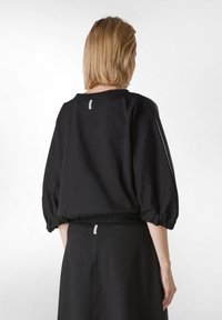 Suéter de algodón negro con un escote ancho y redondeado, mangas abullonadas y cintura elástica. Presenta una pequeña etiqueta con logo en la parte posterior.