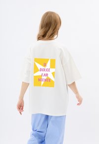 Biała, oversize koszulka z żółtą grafiką w kształcie gwiazdy oraz napisem "IL DOLCE FAR NIENTE" w kolorze różowym. Swobodny krój, luźny fason.