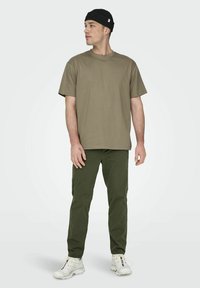 Khaki koszulka z krótkim rękawem zestawiona z oliwkowymi spodniami. Model nosi czapkę z dzianiny w kolorze czarnym i białe buty sportowe. Prosty i casualowy strój.