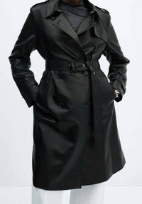 Czarny płaszcz trencz z ekologicznej skóry z paskiem w talii, dwurzędowym zapięciem i dużym kołnierzem; posiada kieszenie i ozdobne guziki.