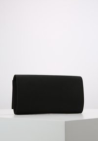 Bolso de mano rectangular negro con una textura mate suave, que presenta un diseño simple de solapa y sin acentos de hardware visibles.