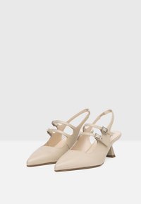 Décolleté beige con punta sottile, due cinturini regolabili e tacco a blocco piccolo. Texture in pelle liscia, design minimal e dettagli metallici.