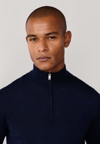 Granatowy sweter zapinany na suwak z wysokim kołnierzem, dzianinowy materiał, slim fit i małe logo na klatce piersiowej. Gładka faktura i minimalistyczny design.