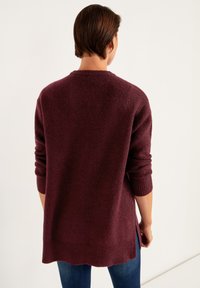 Burgundy neule, jossa on teksturoitu pinta, pyöreä kaula-aukko ja ribbireunat hihoissa ja helmassa. Sivurei'illä varustettu rentoa istuvuutta varten.