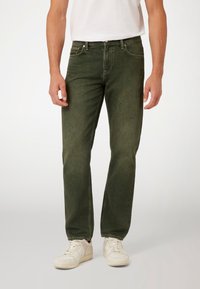 Alyvuogių spalvos džinsai su tiesiu kirpimu, penkiomis kišenėmis ir matomomis siūlėmis. Dėvimi su baltais sportiniais bateliais ir paprastu baltu marškinėliu.