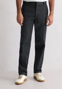 Ciemnoszare spodnie z teksturowanej tkaniny, o prostym kroju nogawek i przednich kieszeniach, zestawione z kremowymi sneakersami.