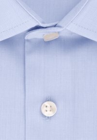 Lichtblauw overhemd met een puntkraag, een enkele witte knop bij de hals en een textuurstof.