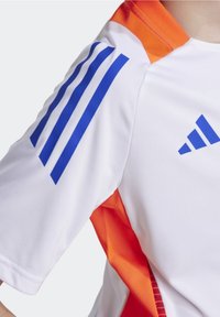 Camisa deportiva de manga corta en blanco y naranja, con un diseño de tres franjas azules en el hombro, con una textura suave y tejido transpirable.
