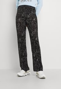 Svarta byxor med vita abstrakta mönster, i avslappnad passform och med en slät textur, tillsammans med vita sneakers.