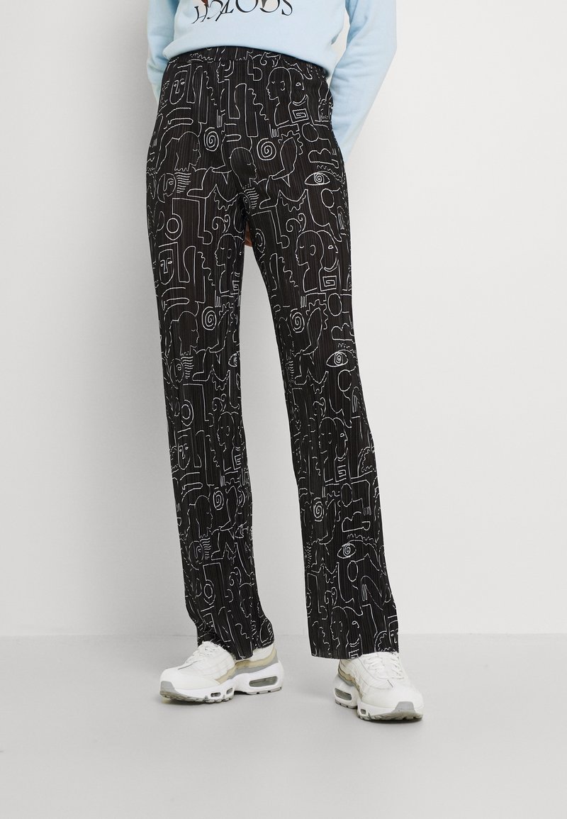 Svarta byxor med vita abstrakta mönster, i avslappnad passform och med en slät textur, tillsammans med vita sneakers.