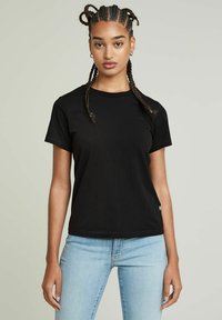 Fekete pamut póló rövid ujjakkal, kerek nyakkivágással és slim fit szabással. Kis címke található az alján és sima textúrájú.