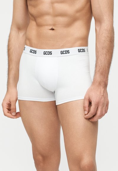 Buste masculin portant un boxer blanc de la marque GCDS avec une ceinture ajustée et aucun motif ou logo visible sur le tissu.