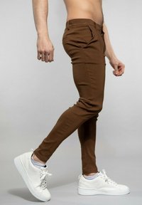 Pantalon moulant marron en tissu stretch, avec des poches latérales et une silhouette slim, associé à des baskets blanches.